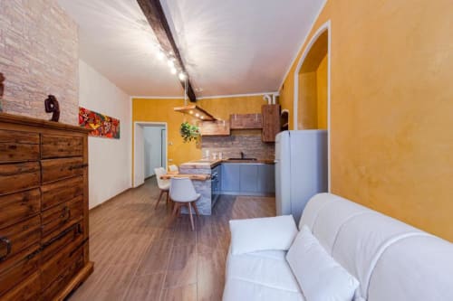 Moderno appartamento a Dimore Verona con pareti gialle, cucina blu, divano bianco, arredi in legno e pavimenti in legno