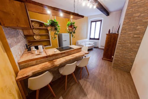 Appartamento Dimore Verona con bancone rustico in legno, sedie color crema, parete gialla, piante sospese e accenti in mattone