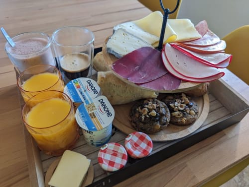 Plateau petit-déjeuner au cottage La Romance à Bagard avec fromages, charcuteries, jus, café et pâtisseries sur table en bois