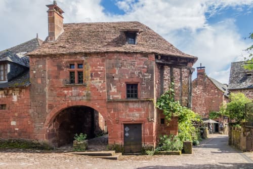 Bâtiment historique en grès rouge avec portail voûté à Darazac, France, architecture traditionnelle et lierre grimpant