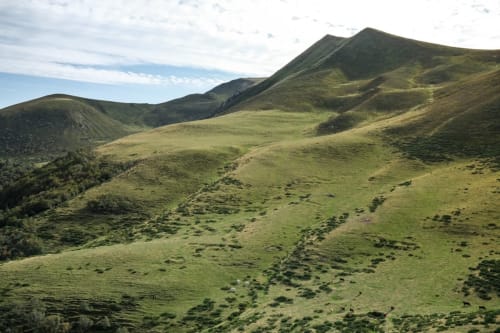 Collines volcaniques verdoyantes et vallées près de Darazac, France avec végétation clairsemée et pics montagneux sous un ciel partiellement nuageux