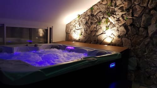 Bain à remous illuminé aux lumières bleues et eau bouillonnante au cottage Accolade à Châteaudun, mur en pierre en arrière-plan