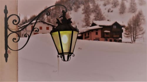 Elegante lanterna da parete illuminata nel suggestivo paesaggio innevato di Livigno con caratteristici edifici alpini rossi