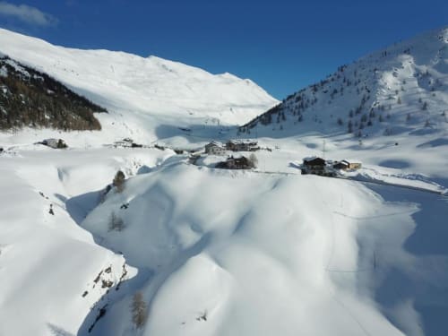 Valle alpina innevata con chalet a Livigno, Italia, circondata da montagne sotto un cielo azzurro