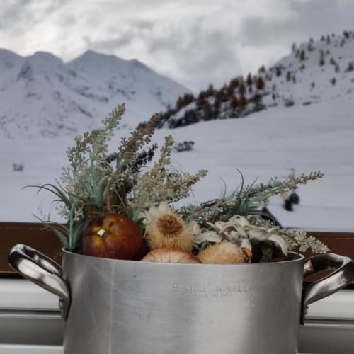 Pentola di metallo con verdure autunnali e erbe secche con vista sulle montagne innevate di Livigno