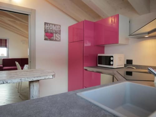 Cucina moderna con mobili rosa acceso, piano di lavoro grigio e vista sulle montagne dell'appartamento Al Dos a Livigno