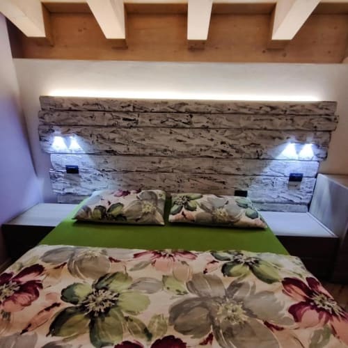 Camera moderna dell'appartamento Al Dos Livigno con testata in legno bianco, biancheria verde e cuscini floreali