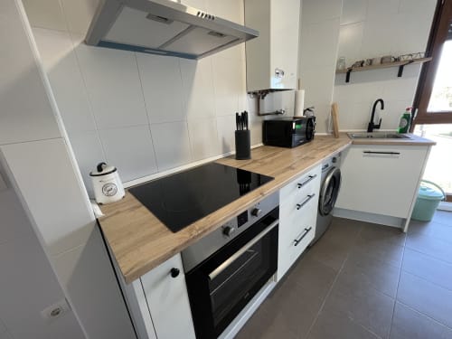 Cocina moderna en apartamento de Salamanca con muebles blancos, encimera de madera, placa de inducción negra y acero inoxidable