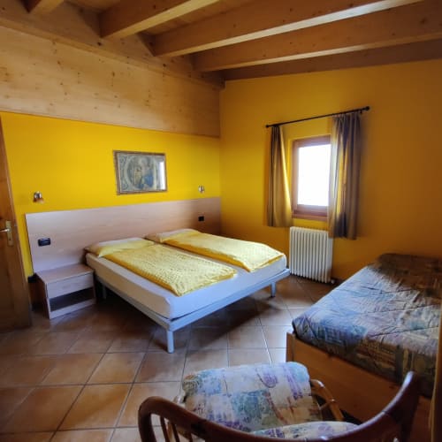Camera da letto giallo brillante dell'appartamento Al Dos a Livigno con letto matrimoniale, vista montagna e soffitto con travi in legno