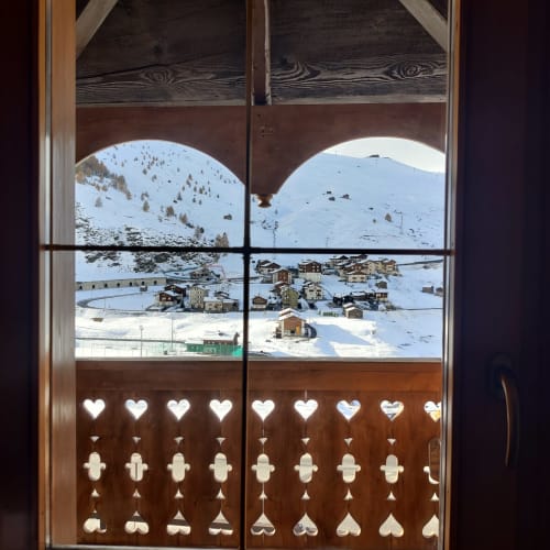 Porta alpina in legno con intarsi di cuore e croce affacciata sul villaggio innevato di Livigno e le cime montane