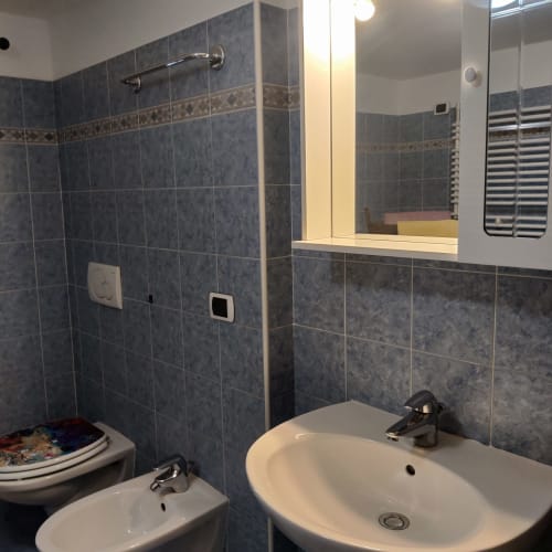 Bagno moderno con piastrelle blu, lavabo bianco, bidet, wc e specchio illuminato all'hotel Al Dos di Livigno