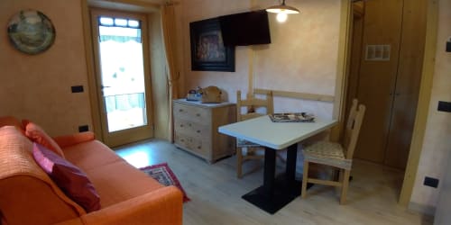 Appartamento al piano terra di Al Dos a Livigno con divano arancione, tavolo da pranzo e accesso al balcone con vista montagna