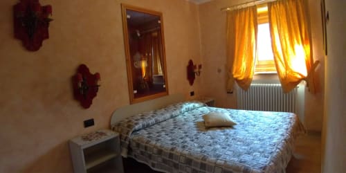 Camera luminosa all'appartamento Al Dos a Livigno con letto matrimoniale, vista montagna attraverso tende gialle e stile alpino tradizionale