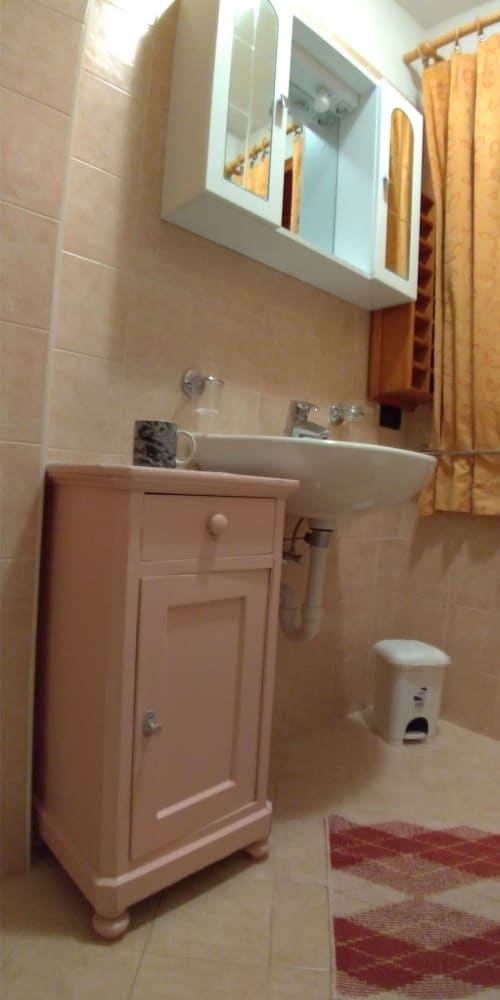 Bagno dell'appartamento Al Dos a Livigno con vanità in legno, lavabo bianco, specchiera e tende dorate