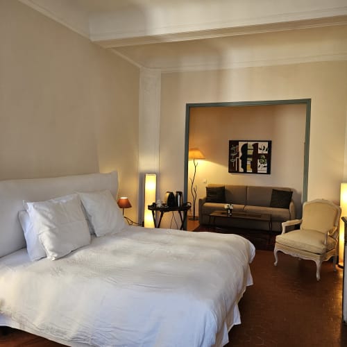 Chambre lumineuse à La Cordeline B&B à Brignoles avec lit blanc, fauteuil crème et coin salon avec vue sur le jardin