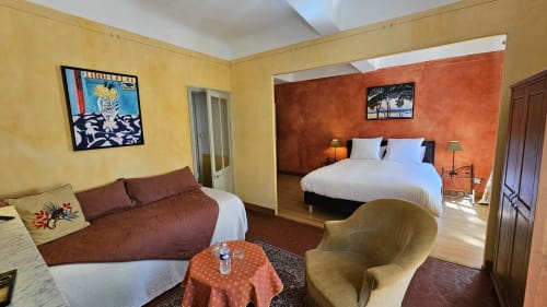 Suite spacieuse à La Cordeline B&B à Brignoles avec murs jaunes et orange, deux lits, fauteuil et vue sur la ville