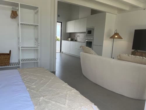 Sala de estar de moderna moradia com sofá curvo branco, cozinha aberta e vistas para a montanha em Bordeira, Portugal