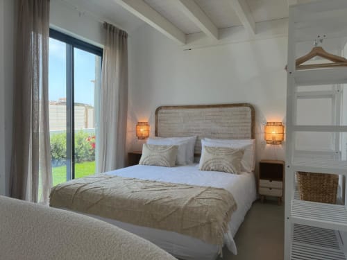 Quarto moderno e luminoso na villa Casa Ingrina, Bordeira, com cabeceira em rattan, roupa de cama branca, iluminação ambiente e vista para a montanha