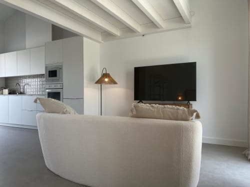Sala de estar moderna da villa Casa Ingrina em Bordeira, com sofá curvo creme, TV inteligente na parede, cozinha branca e acabamentos expostos