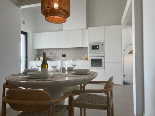 Cozinha e sala de jantar modernas na villa Casa Ingrina, Bordeira, com mesa de mármore redonda, cadeiras de madeira e armários brancos