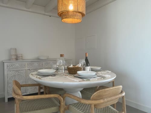 Elegante sala de jantar da villa Casa Ingrina em Bordeira com mesa redonda branca, cadeiras de madeira e luminária de palha trançada.