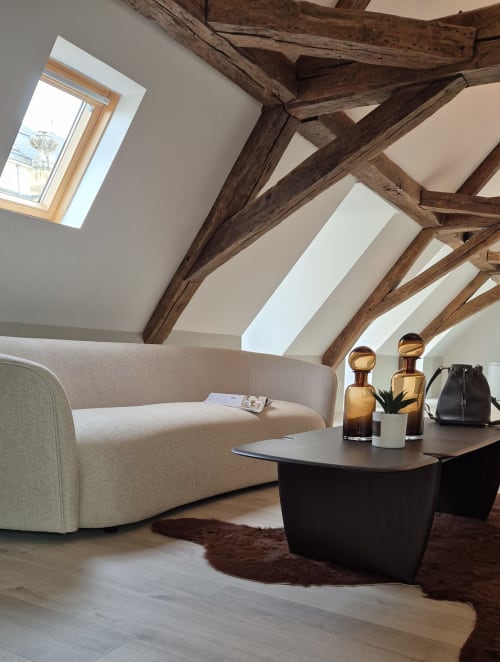 Moderne loftwoning in Moulin Renaudiots met zichtbare houten balken, crème bank, zwarte tafel en dakramen met uitzicht