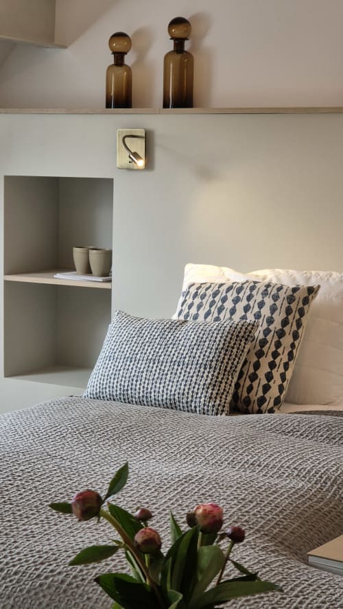 Slaapkamer in Moulin Renaudiots in Autun met gemusterde kussens, amberkleurige flessen op plank en verse bloemen op het bed