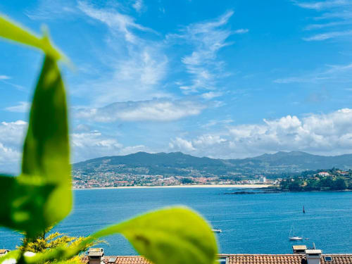 Vista costera de Baiona desde el jardín de la casita Holibai, con vistas al mar azul, playa, montañas y veleros
