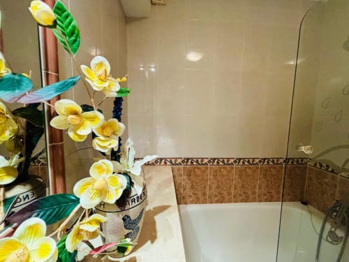 Baño moderno de la casa rural Xoaniña en Baiona, con orquídeas amarillas, ducha a ras de suelo y revestimientos decorativos
