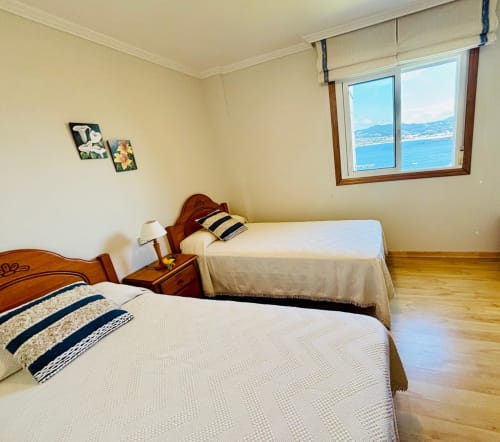 Dormitorio luminoso con camas gemelas, vistas al mar de Baiona, muebles de madera y ropa de cama a rayas en apartamento de cabaña costera