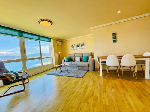 Luminoso apartamento junto al mar en Baiona con suelos de madera, sofá gris, vistas al océano y mobiliario moderno