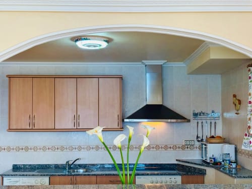 Cocina moderna en cottage de Baiona con armarios de madera, encimera negra, calas blancas y campana extractora de acero inoxidable
