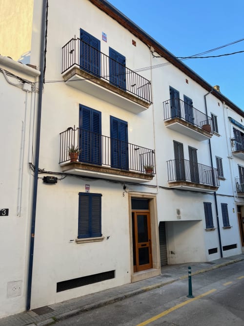Historic apartment building in Palafrugell with blue shutters, balconies, and wooden entrance door on a quiet street