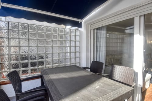 Modern terrace with outdoor dining furniture, glass block wall, and sliding glass doors at Calella apartment in Palafrugell