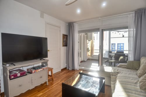 Bright living room in Calella apartment with TV, balcony doors, striped sofa, and wooden floors