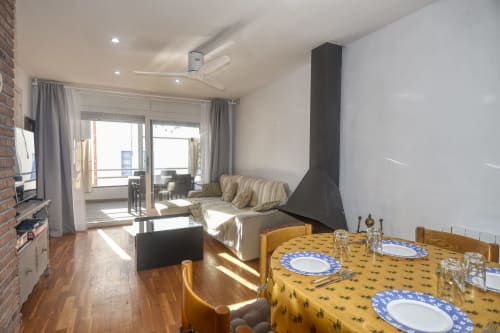 Modern apartment dining and living area in Calella with fireplace, coastal views, wooden table, and contemporary furnishings