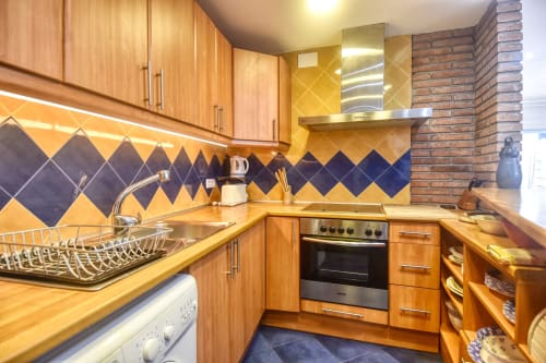 Modern kitchen with wood cabinets, yellow and navy diamond backtile, stainless steel oven and range hood at Finques Garcia