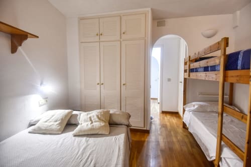 Bright apartment bedroom in Calella with single bed, wooden bunk beds, cream wardrobe, and wooden flooring