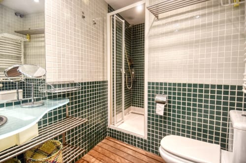 Modern bathroom with dark green and cream tile work, shower enclosure, vanity sink, and heated towel rack in Calella
