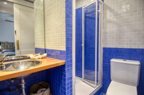 Modern blue and white bathroom with wooden sink vanity, glass shower enclosure, and toilet in Calella apartment