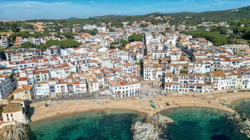 Aerial view of Calella beachfront in Palafrugell, Spain with colorful buildings, sandy beach, and turquoise Mediterranean Sea