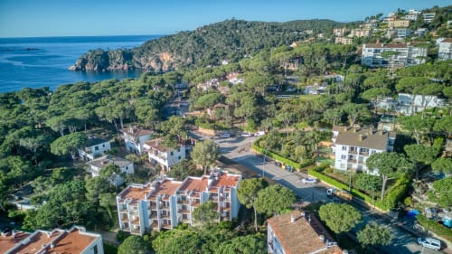 Aerial view of Palafrugell coastal apartment complex with Mediterranean sea, terracotta buildings, and pine forest