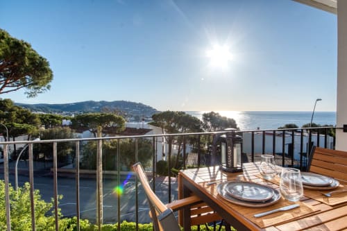 Coastal apartment terrace in Palafrugell with dining table, sea views, and Mediterranean trees under bright sunshine