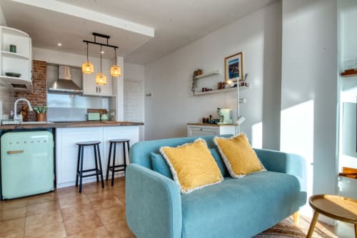 Modern apartment kitchen and living area with turquoise sofa, yellow pillows, and sea view in Palafrugell