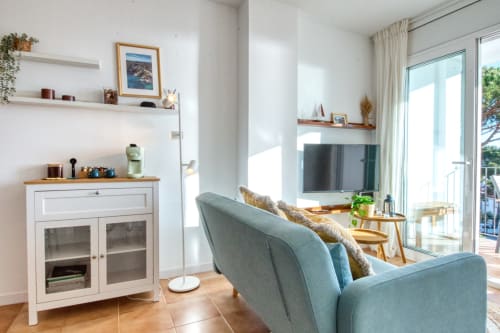 Modern apartment living room in Palafrugell with sea views, blue sofa, TV, white storage cabinet, and bright natural light