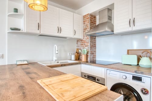 Modern kitchen in Palafrugell apartment with white cabinetry, wood counters, brick chimney, and induction cooktop