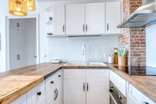 Modern kitchen in Palafrugell apartment with white cabinets, wood countertops, and exposed brick wall