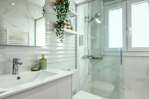 Modern bathroom in Palafrugell apartment with marble tiles, glass shower enclosure, and hanging plant decor
