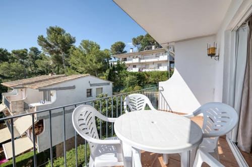 Balcony with white table and chairs overlooking trees at Finques Garcia Enrich apartment in Palafrugell