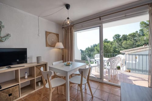Modern apartment dining area in Palafrugell with sea views, white table, wooden chairs, and balcony access overlooking the
